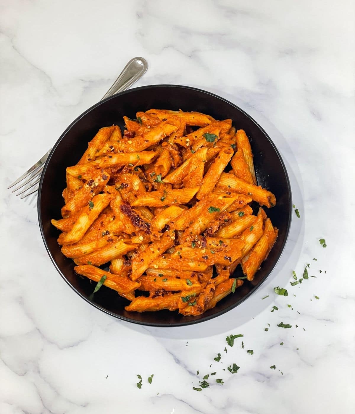 A plate of vegan sun dried tomato pasta is on the table along with fork.