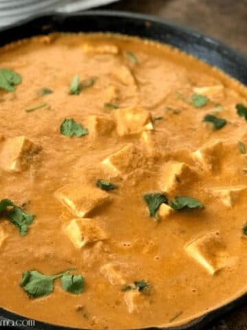 A cast iron pan is filled with tofu butter masala curry and topped with cilantro