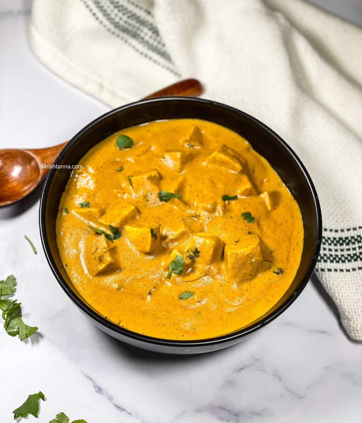 A bowl of vegan tofu paneer butter masala is on the table.