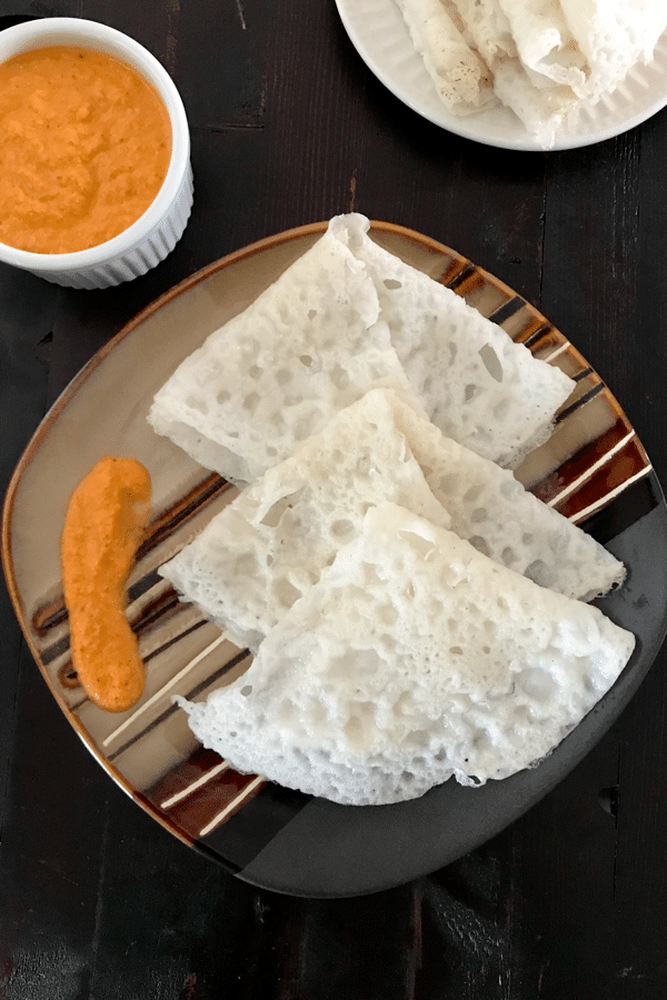 A plate of neer dosa and red chutney is on the table