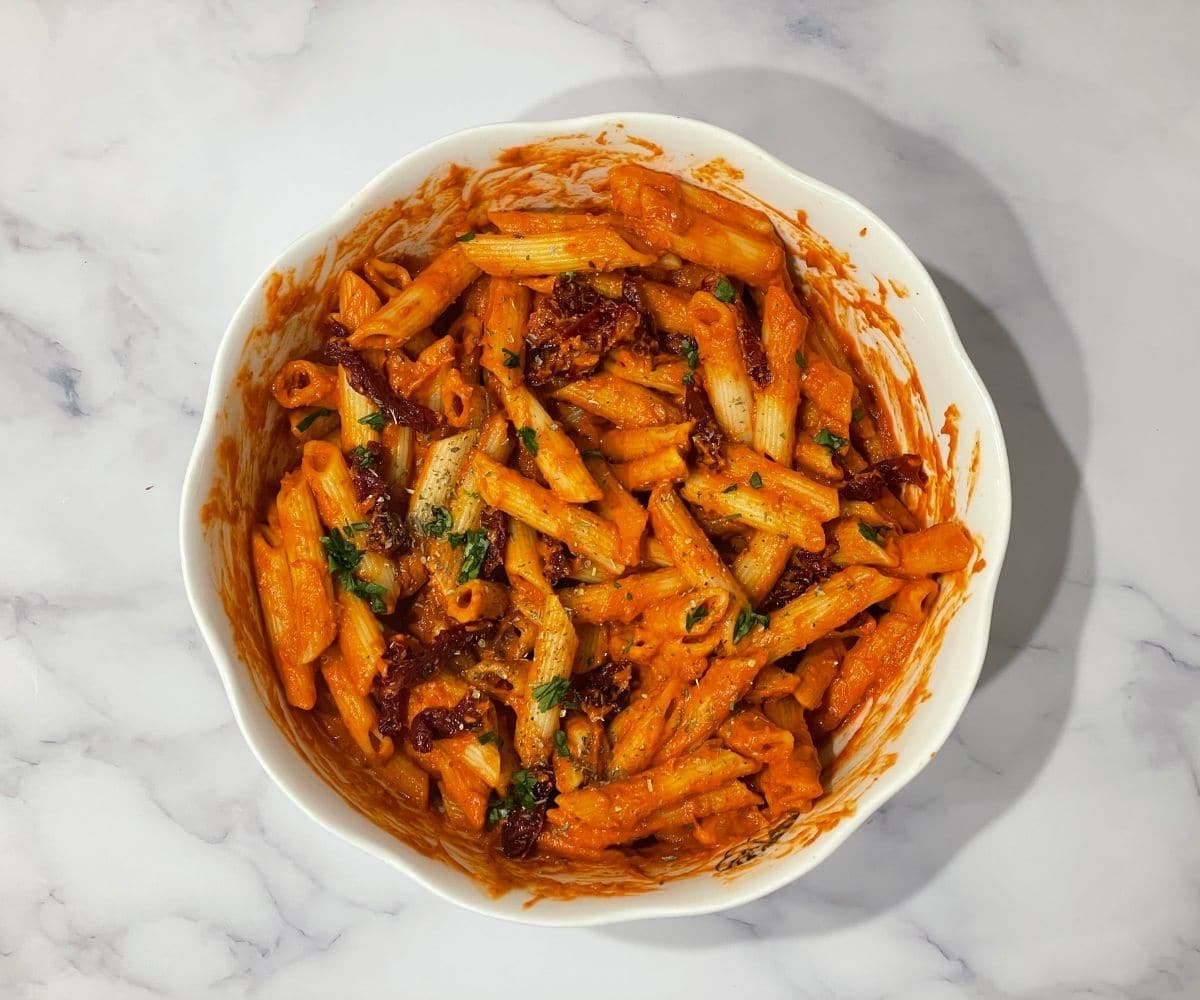 A bowl of vegan sun dried tomato pasta is on the table.