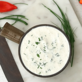 A bowl of food on a plate, with Ranch dressing and Chives