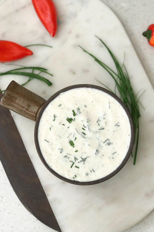 A bowl of food on a plate, with Ranch dressing and Chives