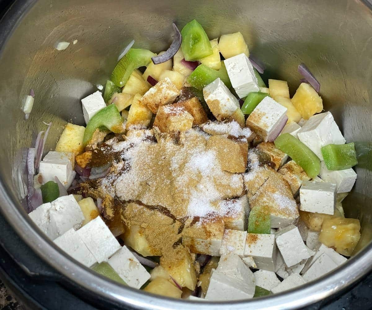 An instant pot is filled with pineapple cubes, bell pepper, and tofu for pineapple fried rice.,