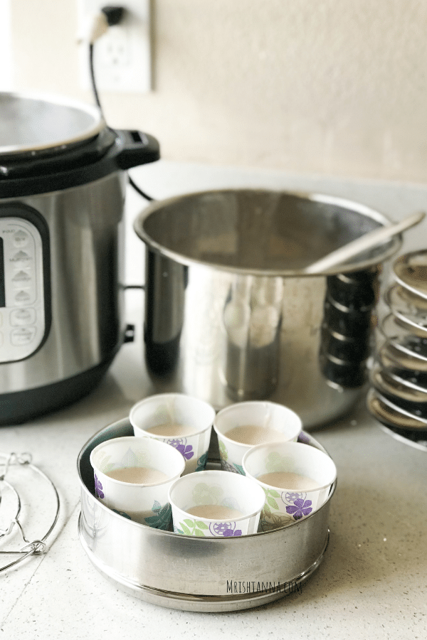A steel pot is with idli batter filled with paper cups.