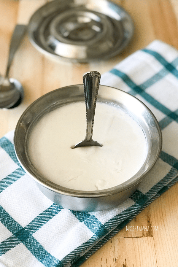 A steel bowl filled with coconut milk curd with spoon