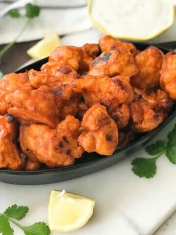 A bowl is with cauliflower buffalo wings and lemon is on the side