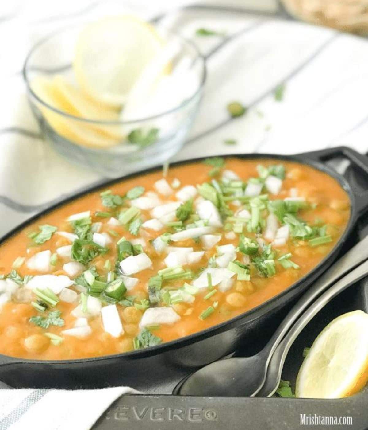 A iron serving bowl is with instant pot matar chaat and topped with chilies and cilantro.