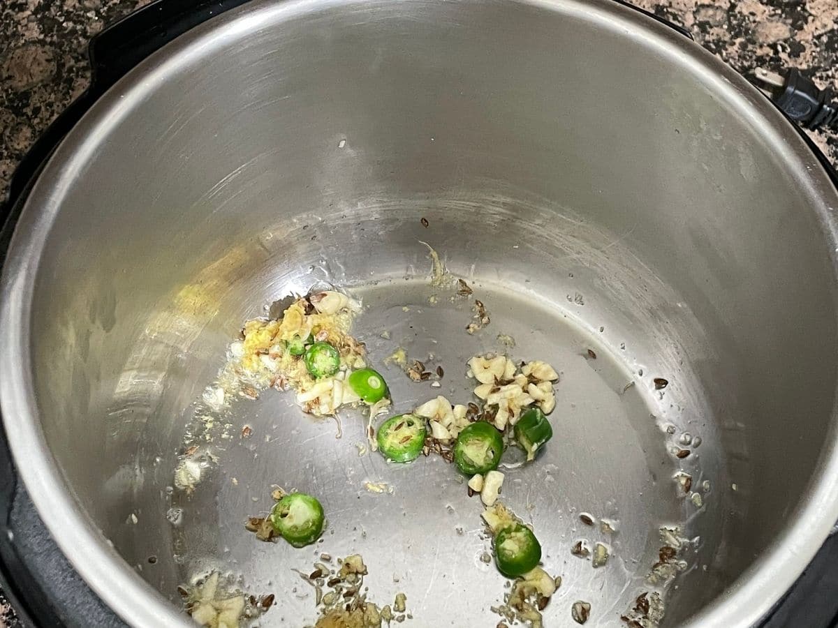 An instant pot is with oil, cumin seeds and green chilies on cooking mode