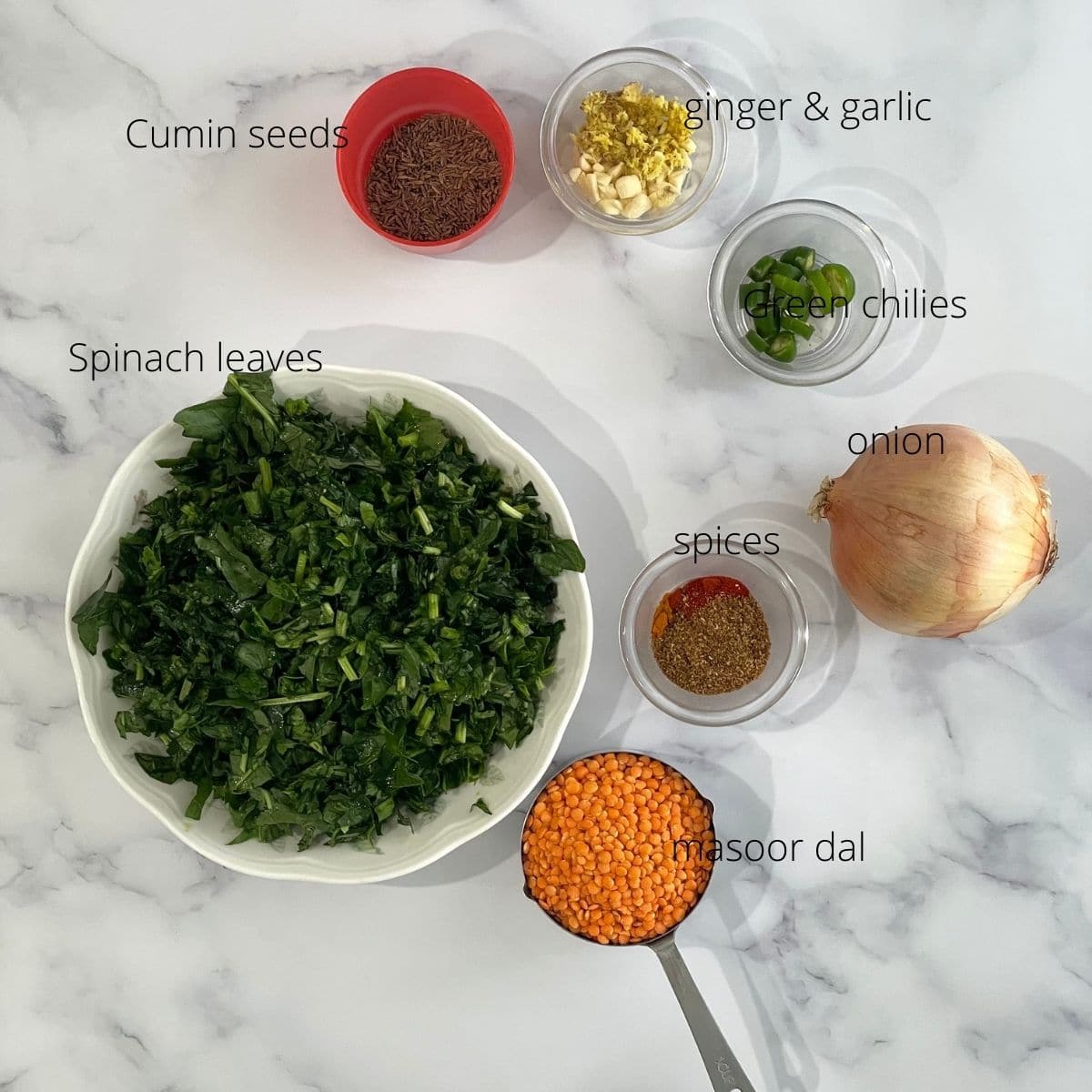 Spinach, onion, cumin seeds, and red lentils are on the table for dal recipe.