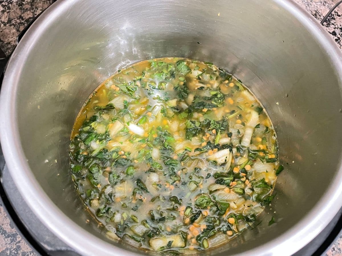 An instant pot is with uncooked spinach and lentils