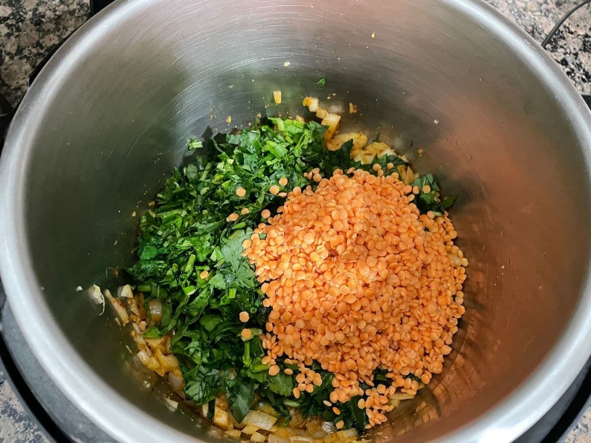 An instant pot is with chopped spinach and lentils for dal