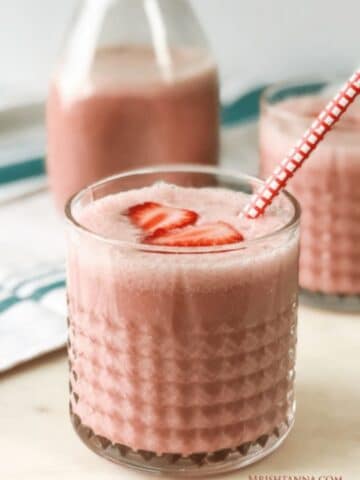 A glass is with strawberry lassi and straw is inserted.