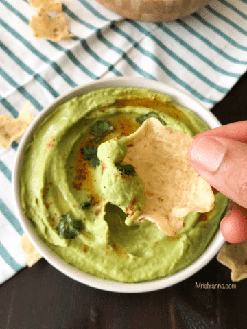 A person holding chips with hummus