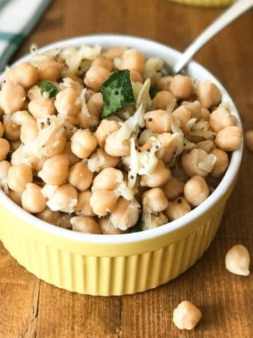 A bowl of chickpeas salad is on the table with spoon inside