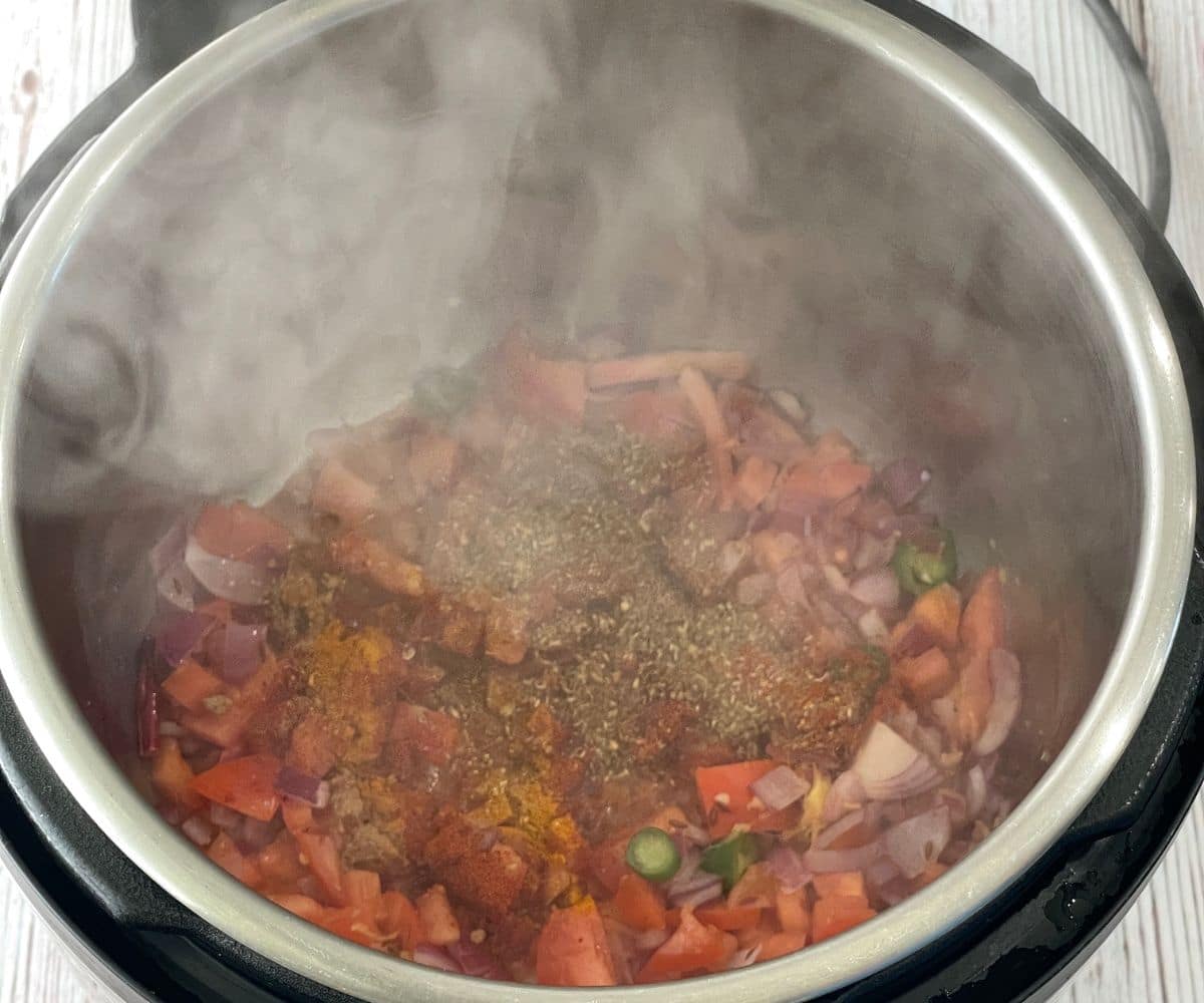 An instant pot is with tomatoes and spices.