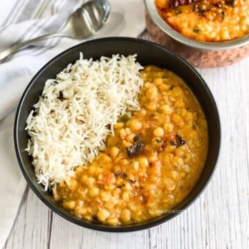 A bowl of chana dal and rice is on the table with a spoon by the side.
