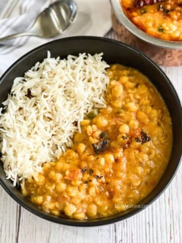 A bowl of chana dal and rice is on the table with a spoon by the side.