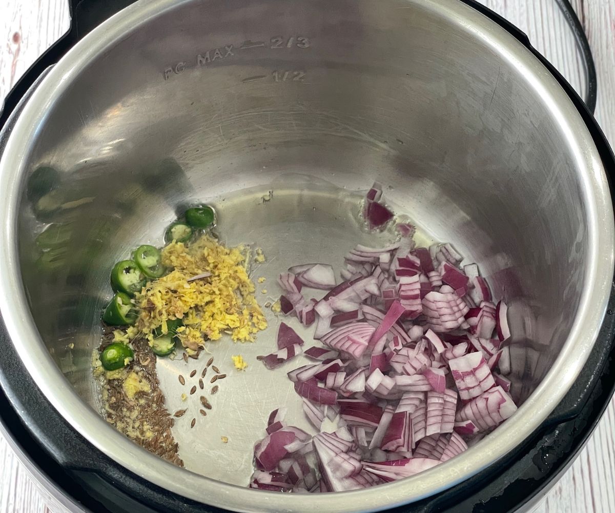 An instant pot is with oil, spices and chopped onions on saute mode.