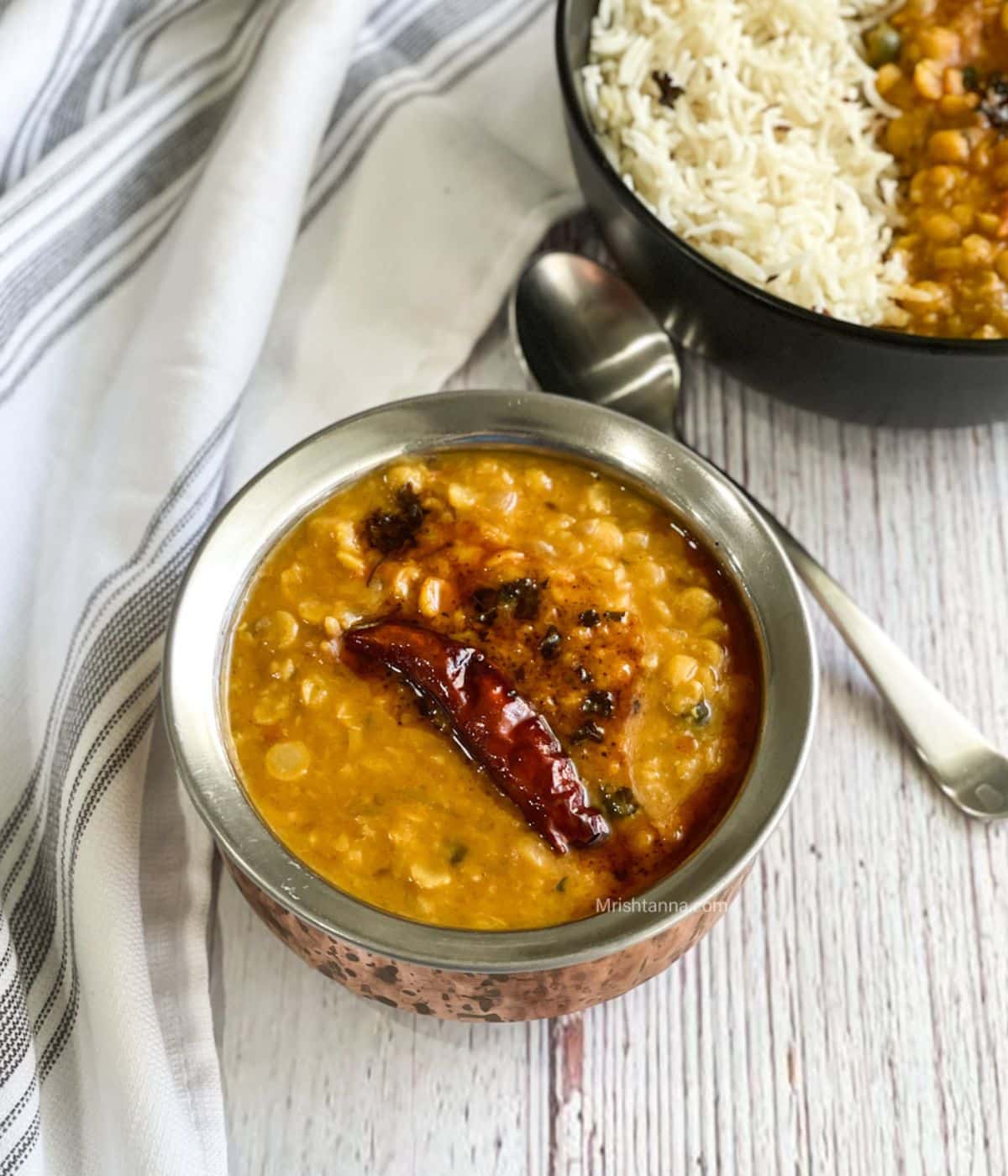 A copper bowl is with chana dal and topped with tadka.