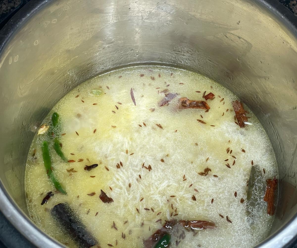 A pot has rice, water and spices for cumin rice.