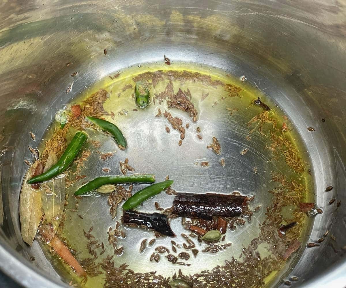 An Instant pot has wholes spices and green chilies.