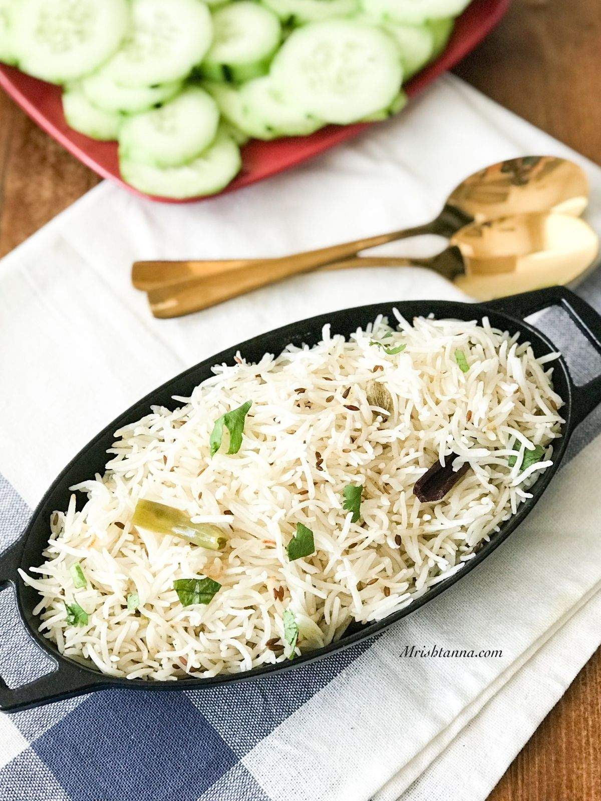 A black iron pot is filled with jeera rice and its on the table with golden spoon