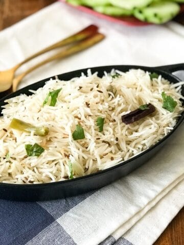 A black iron pot is filled with jeera rice and its on the table with golden spoon