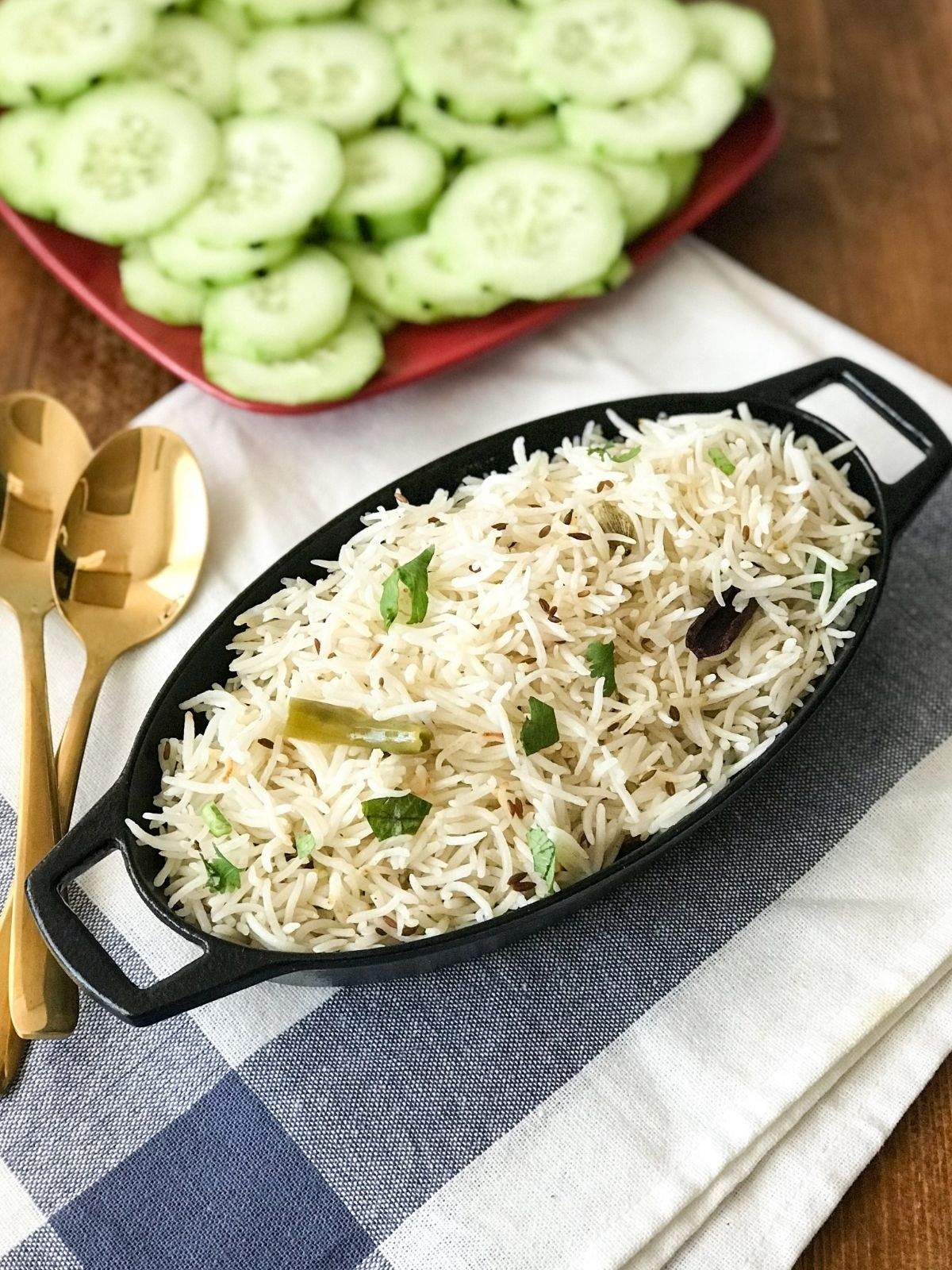 A black iron pot is filled with jeera rice and its on the table with golden spoon