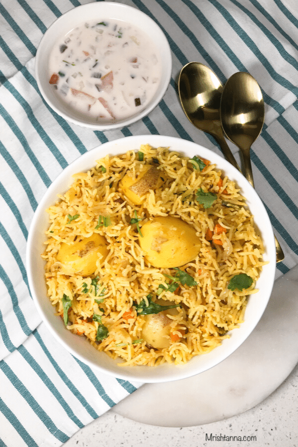 A plate of aloo biryani is on the table with, golden spoons