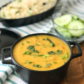 A black bowl filled with dal along with sliced cucumber
