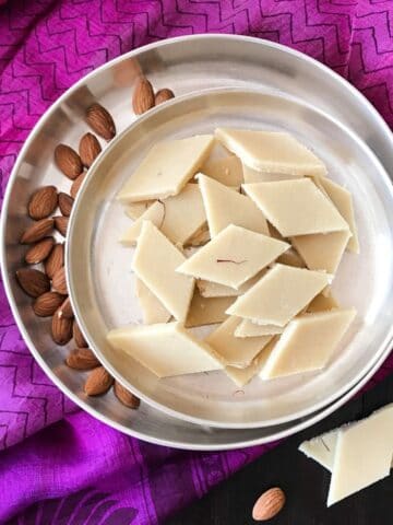 A silver plate is with badam bufi and whole almonds are kept on the side