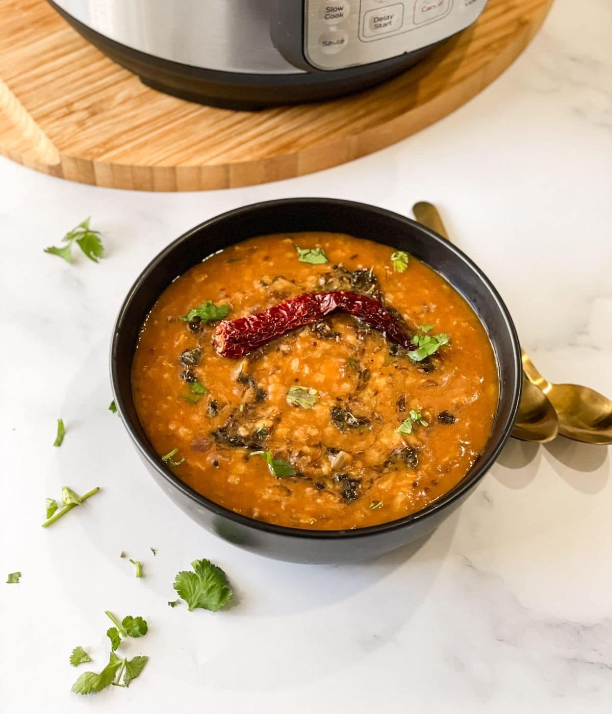 A bowl of dal tadka is on the table and topped with cilantro  and chilli.