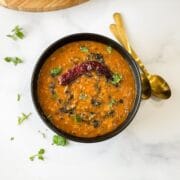 A bowl of dal tadka is on the white table.