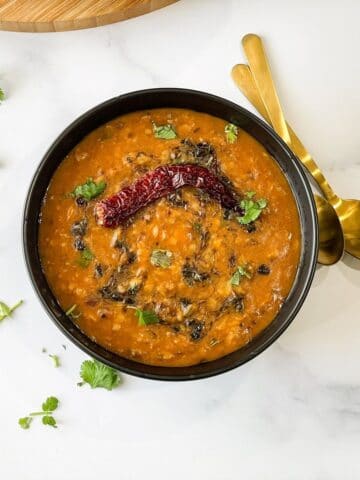 A bowl of dal tadka is on the white table.