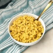 a bowl of vegan mac and cheese is placed on the table with golden fork.