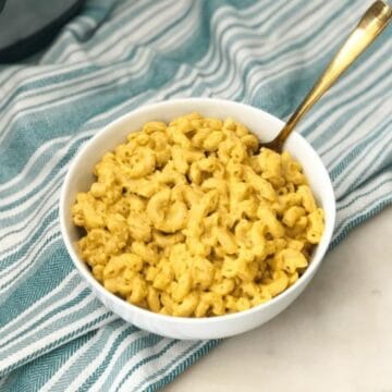 a bowl of vegan mac and cheese is placed on the table with golden fork.