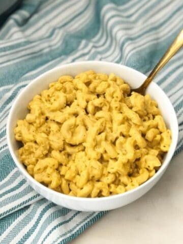 a bowl of vegan mac and cheese is placed on the table with golden fork.