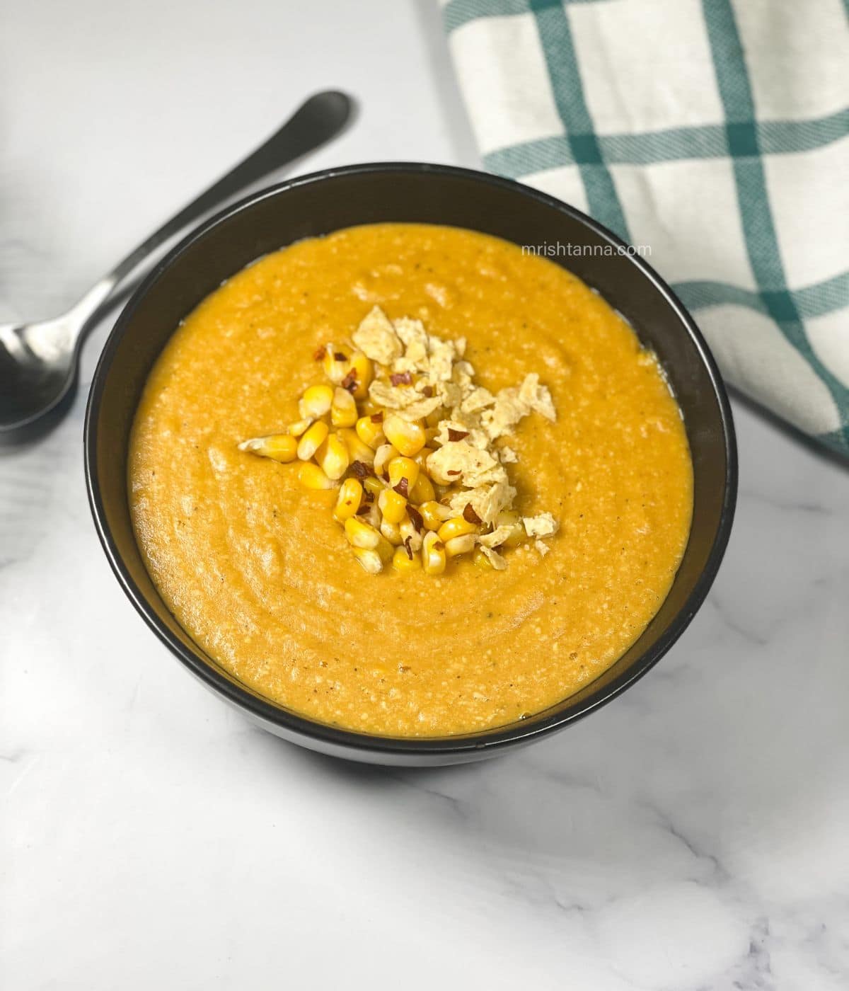 A bowl is filled with vegan corn chowder and topped with corns.