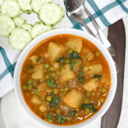 A bowl of aloo matar curry with a side of cucumber