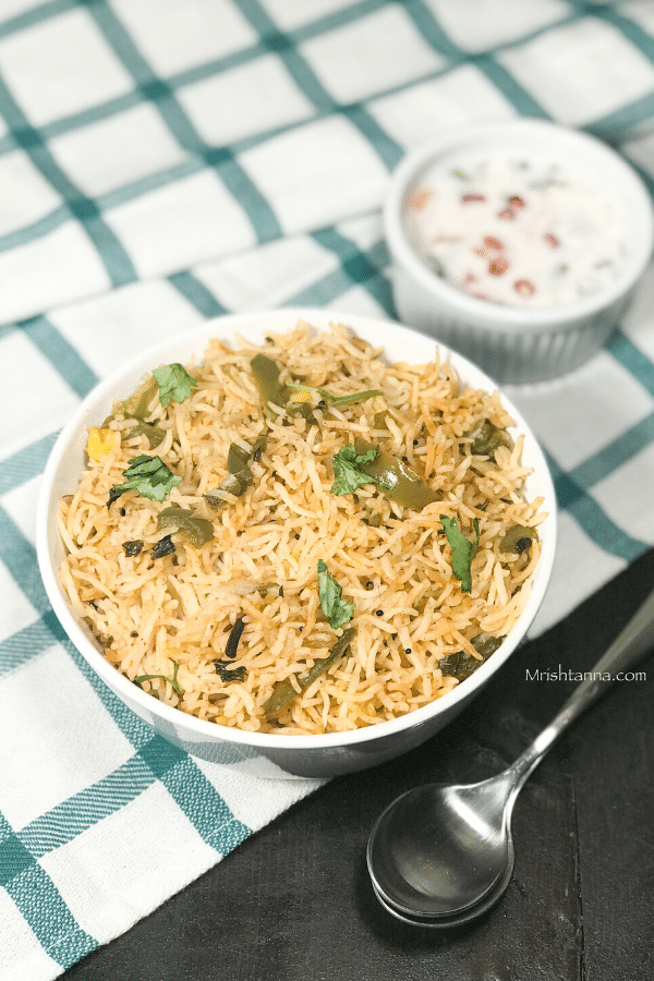 A bowl of capsicum rice on the table along with raita
