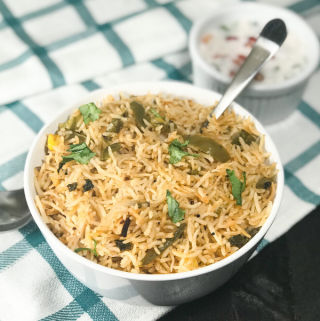 A white bowl filled with bell pepper rice and spoon is placed