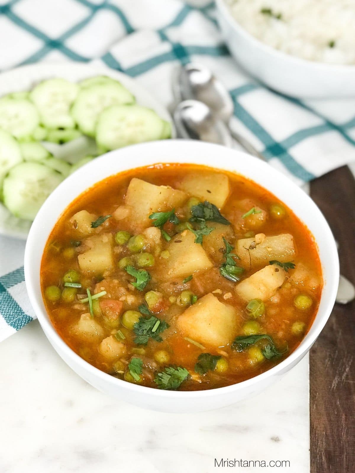 A bowl of aloo matar curry is on the white board.