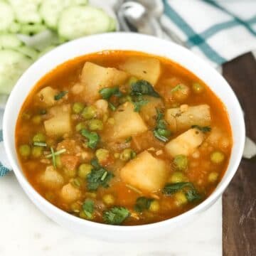 a bowl is with aloo matar curry and placed on the white serving tray