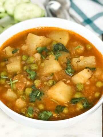 a bowl is with aloo matar curry and placed on the white serving tray