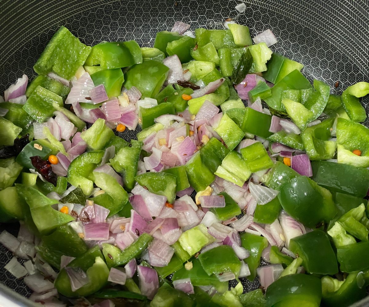 A pan is with chopped onions and capsicum over the heat.