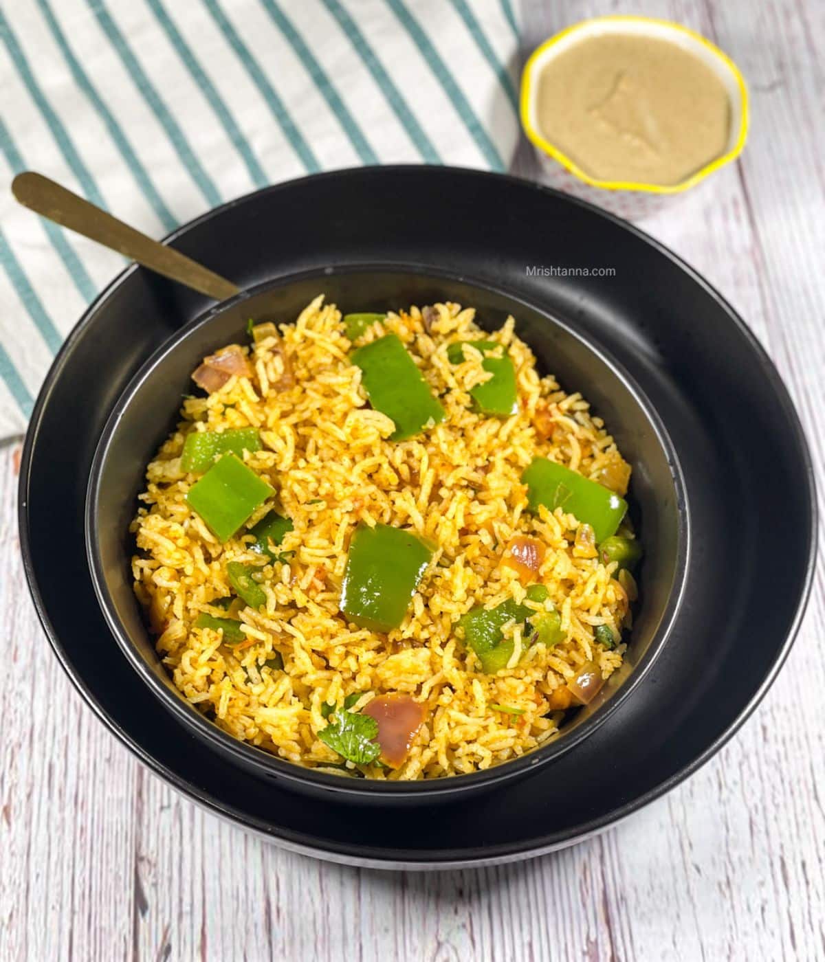 A bowl of bell pepper rice is on the plate with a golden spoon.