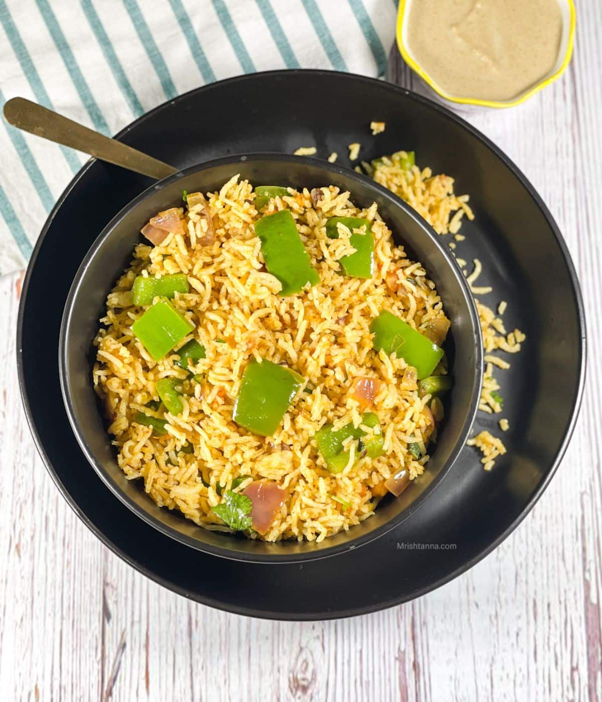 A plate is with bowl of capsicum rice and a spoon.