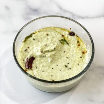 A glass bowl is with coconut chutney on the table.