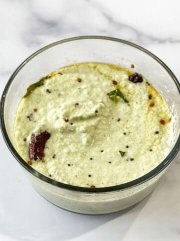 A glass bowl is with coconut chutney on the table.